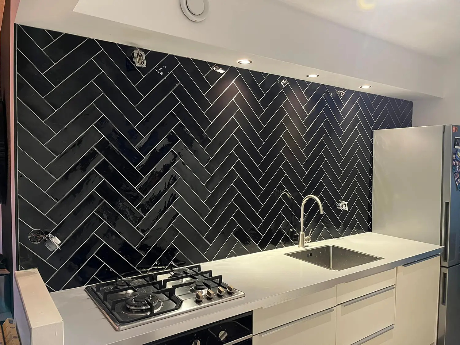 Keukenrenovatie voor en na, met zwarte glans tegels in visgraad motief gebruikt bij deze keuken renovatie